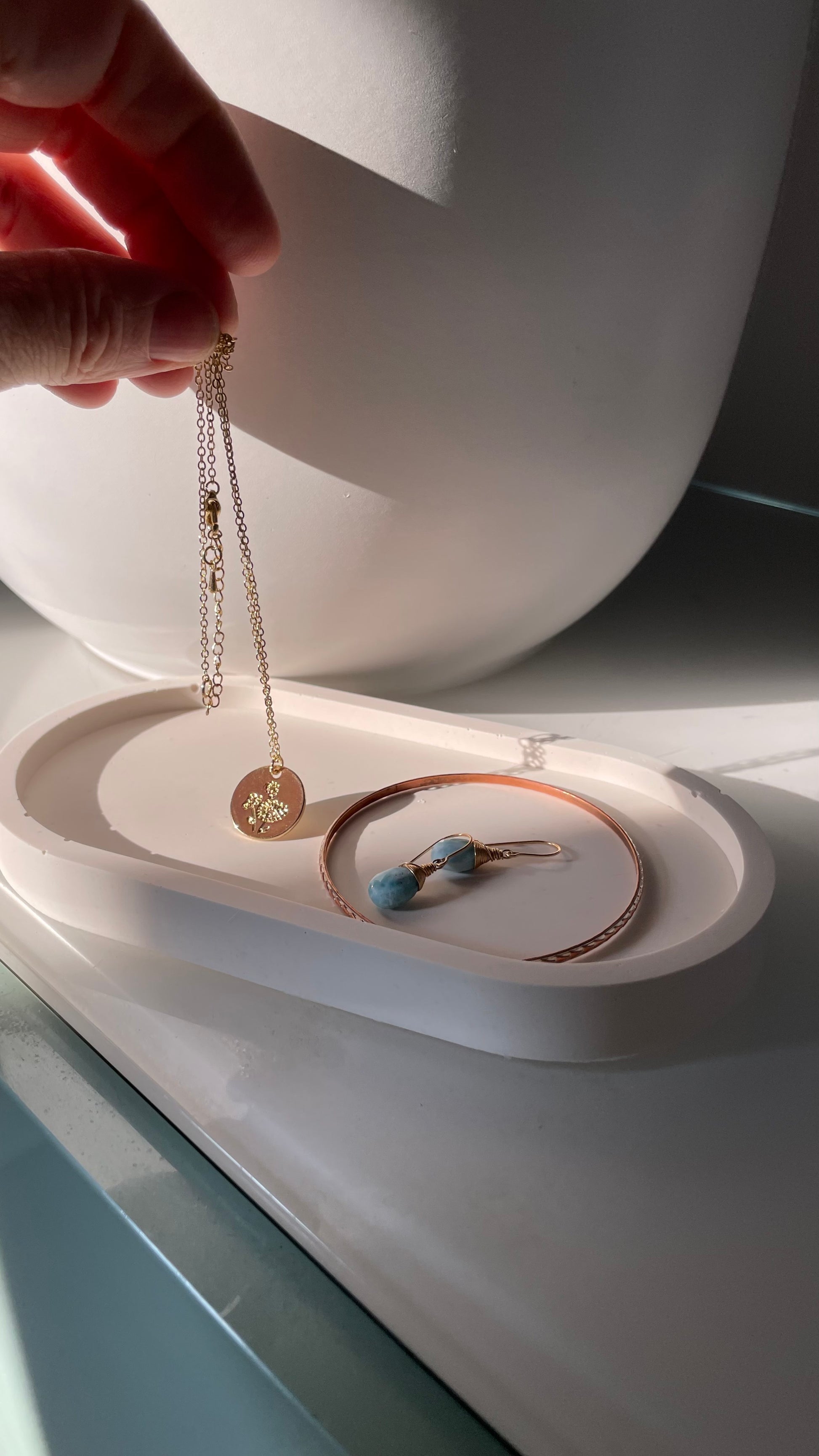 A hand is reaching to add jewelry to a white oval tray.